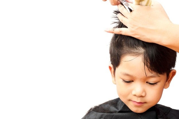 เด็กผมสีดำกำลังมองลงขณะที่ผู้ใหญ่กำลังตัดผมด้วยกรรไกรและหวี โดยมีพื้นหลังสีขาว